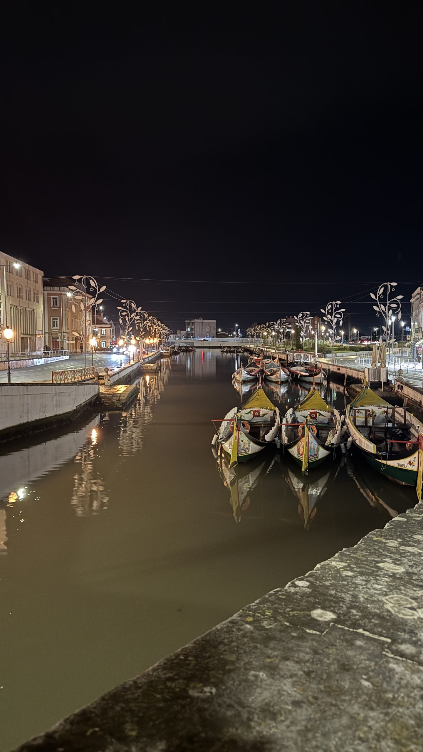 Moliceiro boats on Aveiro canal at night with reflections of city lights